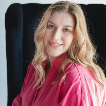 Portrait of a smiling woman in a pink shirt sitting indoors.